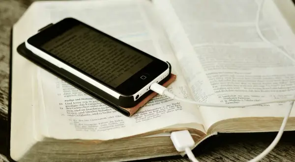 Nowoczesna biblia na co dzień: smartfon z tekstem biblijnym leży na otwartej księdze, podłączony do ładowania.
