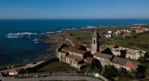 Monasterio de Santa María de Oia, con su torre campanario y tejados rojizos, se alza majestuoso junto al mar Cantábrico.