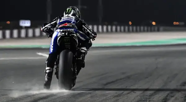 Piloto de MotoGP en plena acción, buscando el holeshot. La moto levanta polvo al acelerar en la noche.