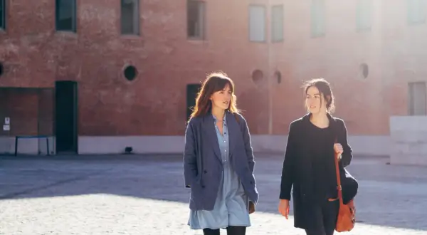 Las hermanas Arce caminan juntas bajo el sol, conversando animadamente frente a un edificio de ladrillo.