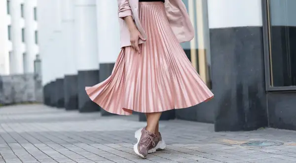 Gonna plissettata rosa cipria, un outfit inverno chic con blazer e sneakers.
