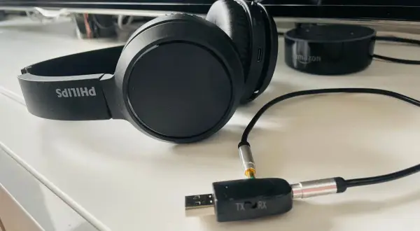Czarne słuchawki Philips podłączone do adaptera Bluetooth TX/RX na białym blacie.