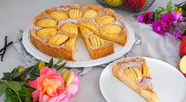 Ein sensationelles Apfeltarte-Rezept: goldbrauner Boden, saftige Äpfel, Puderzucker. Daneben eine Rose und Äpfel im Korb.