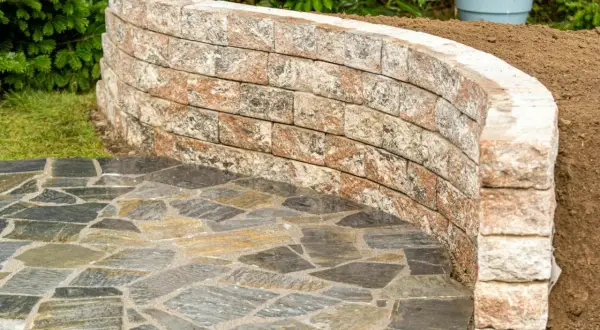 Muretto curvo in pietra per giardino, con pavimentazione irregolare in ardesia. Belle idee per muretti da giardino.