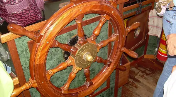 Il timone, come si chiama il volante della nave, è di legno lucido, pronto a guidare.