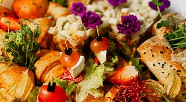 Pyszne przekąski na 18. urodziny: mini croissanty, tartinki z pomidorkami i serem, roladki z tortilli, truskawki i dekoracje z kwiatów.