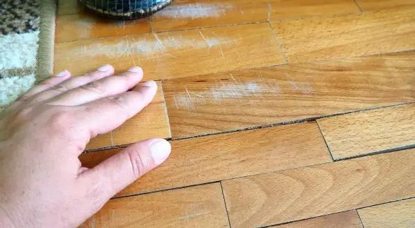 Mano sul parquet graffiato, un problema comune per chi vuole sapere come togliere strisciate scarpe dal parquet.