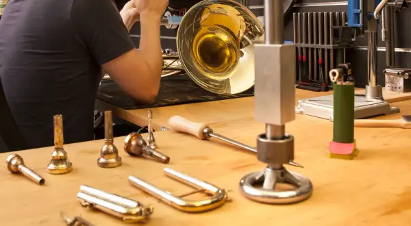 Werkstatt für Blasinstrumente Reparatur: Ein Mann arbeitet an einem glänzenden Horn, Werkzeuge und Mundstücke liegen bereit.
