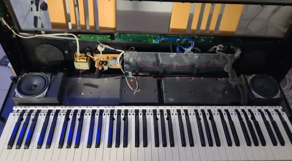 Wnętrze keyboardu podczas naprawy. Widoczne głośniki, płytki drukowane, kable i klawisze.