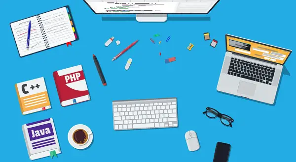 Kobieta programistka przygotowuje się do nauki. Na biurku książki: C++, PHP, Java, laptop, monitor, klawiatura, myszka, okulary, telefon i kawa.