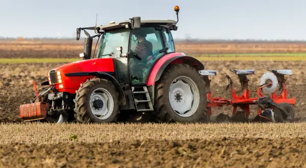 Czerwony traktor z pługiem orze pole. Rolnik przygotowuje ziemię, kiedy orka zimowa jest w pełni.