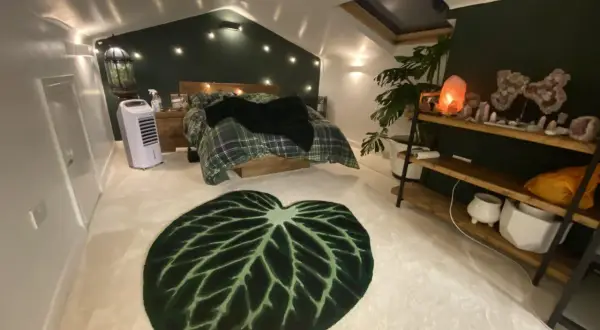 Sovrum med mysig cottage core-känsla. Rutiga sängkläder, gröna väggar och en stor bladmatta. Kristallampor och växter skapar en drömsk atmosfär.