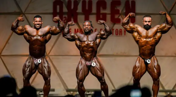 Drei Bodybuilder präsentieren ihre Muskeln auf der Bühne des Mr. Olympia Open.