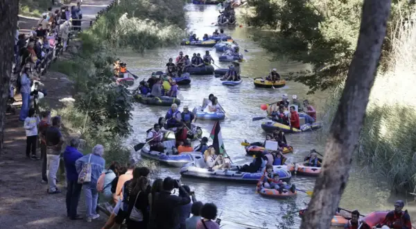 Gente en balsas y kayaks disfrutan de la bajada del canal, rodeados de espectadores en la orilla.