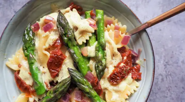 Makaron farfalle z zielonymi szparagami, suszonymi pomidorami i czerwoną cebulą w kremowym sosie.