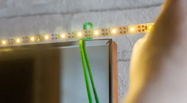 Montaż taśmy LED za lustrem: zielony kabel i świecące diody tworzą subtelne oświetlenie.