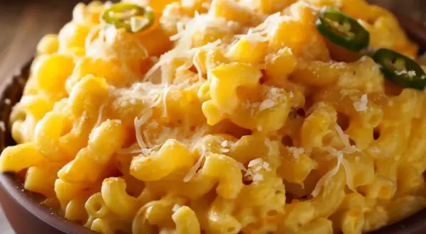Cremiges Mac and Cheese mit Jalapeño-Scheiben und geriebenem Käse, serviert in einer braunen Schüssel.