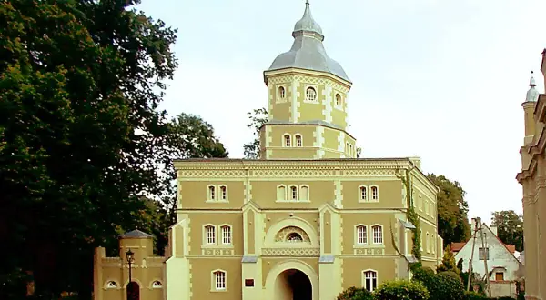 Pałac w Golejewku, z charakterystyczną wieżą i bramą wjazdową, otoczony zielenią.