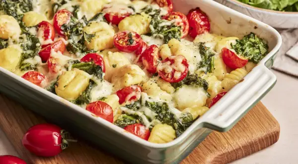 Gnocchi Spinat Auflauf mit Kirschtomaten und geschmolzenem Käse in einer grünen Auflaufform.