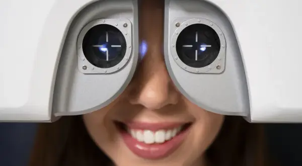 Uśmiechnięta kobieta podczas badania wzroku za pomocą urządzenia optometrycznego.