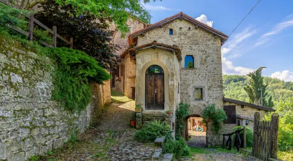 Un vicolo lastricato conduce a un antico portone in legno. La scola di pietra, con edera rampicante, sembra uscita da un libro di fiabe.