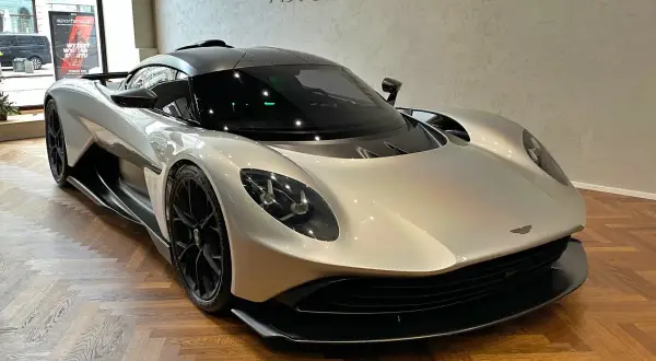 Srebrny Aston Martin na drewnianej podłodze. Zastanawiasz się nad aston martin cena?
