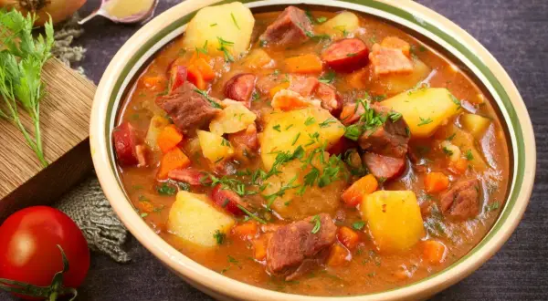Gęsta zupa gulaszowa z ziemniakami, mięsem i kiełbasą, posypana natką pietruszki.