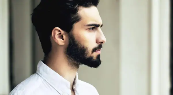Profil d'un homme avec une barbe haute sur les joues, portant une chemise blanche.