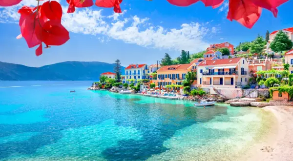 Kefalonia co zobaczyć: malownicza zatoka z turkusową wodą, kolorowe domki na wzgórzu i kwitnące bugenwille. Idealne miejsce na wakacje.