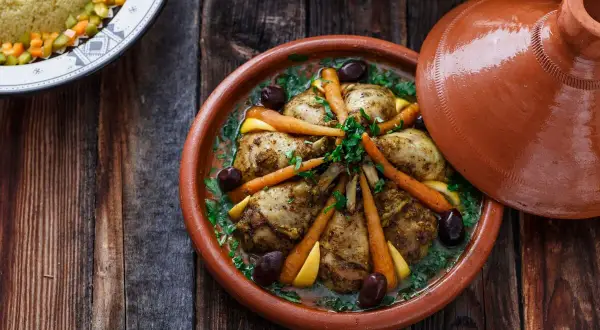 Ein Hähnchen-Tajine mit Karotten, Oliven und Zitrone, serviert in einem traditionellen Tontopf.