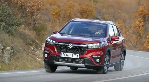 Röd Suzuki S-Cross kör på en kurvig väg i höstlandskap. En man med solglasögon kör bilen under en suzuki s-cross test.