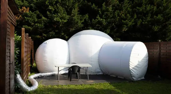 Une bulle gonflable blanche, prête pour une nuit insolite en Île-de-France, est installée dans un jardin verdoyant.