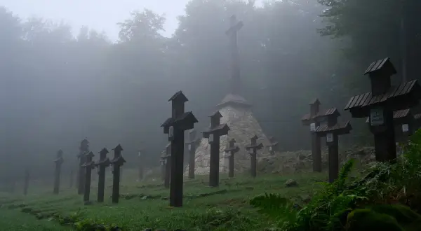 Mglisty poranek na cmentarzu wojennym na Magurze Malastowskiej. Drewniane krzyże stoją w szeregach, a w tle wznosi się monumentalny pomnik.