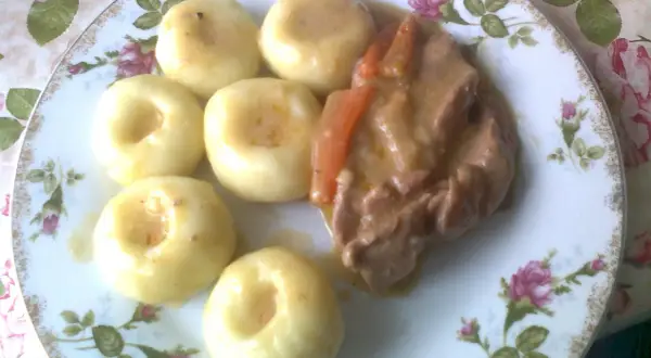 Na talerzu z różanym wzorem ułożone są kluski z mięsem w sosie.
