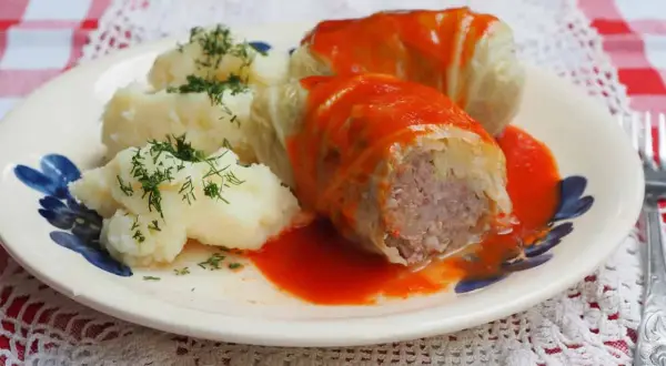 Gołąbki z kapusty włoskiej, podane z purée ziemniaczanym i polane sosem pomidorowym, ozdobione koperkiem.