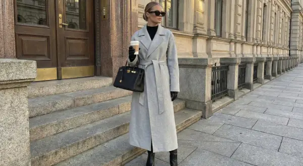 Elegancki szary płaszcz z paskiem, połączony z czarnymi kozakami i torebką, tworzy stylowy look.