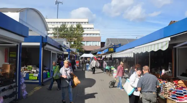 Tętniący życiem rynek we Wrzeszczu, gdzie ludzie spacerują między straganami z obuwiem i odzieżą.