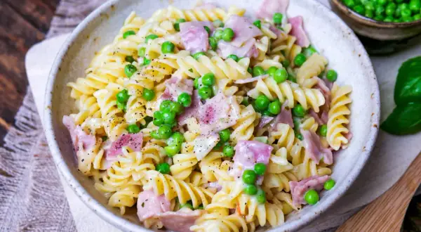 Eine cremige Nudel Schinken Pfanne mit Erbsen und frisch gemahlenem Pfeffer, serviert in einer rustikalen Schüssel.