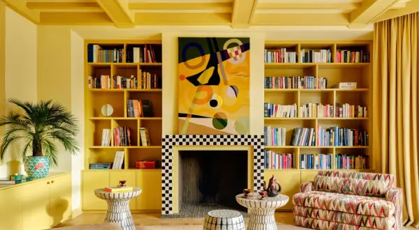 Ein Wohnzimmer in einem gelben Farbrausch, mit Bücherregalen, einem Kamin und einem bunten Sofa.