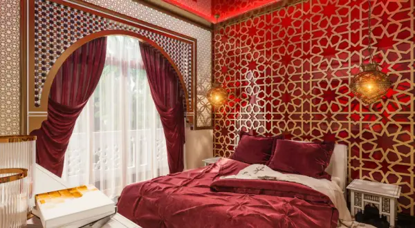 Luksusowa sypialnia w stylu marokańskim. Czerwone ściany z geometrycznymi wzorami, bogato zdobione łóżko i orientalne lampy tworzą magiczną atmosferę.