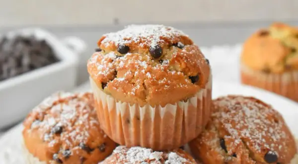 Pyszne muffinki z kawałkami czekolady, posypane cukrem pudrem, kuszą swoim wyglądem. Idealne na deser!