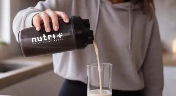 Frau gießt pflanzliches Protein aus einem Shaker in ein Glas. Informiere dich über mögliche proteinpulver nebenwirkungen.