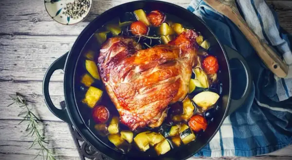 Knusprige putenoberkeule im Bräter mit Gemüse, Tomaten und Kräutern.