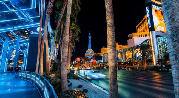 Nocne Las Vegas atrakcje: palmy, neonowe światła, wieża Eiffla i ruch uliczny.
