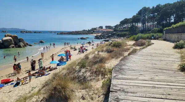 Gente disfrutando del sol y el mar en la playa Pedras Negras. Un camino de madera bordea la arena dorada y las dunas.