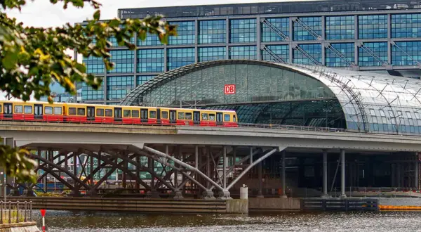 Ein roter und gelber Zug fährt über eine Brücke vor dem Berliner Hauptbahnhof. Die Verbindung Berlin Dresden ist hier gut sichtbar.