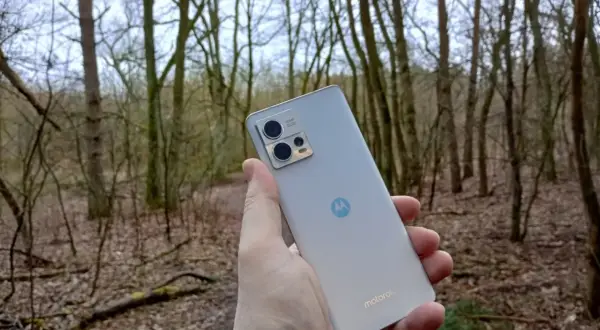 Dłoń trzyma srebrny smartfon Motorola G13 na tle lasu. Sprawdź motorola g13 dane techniczne, by poznać jego możliwości.