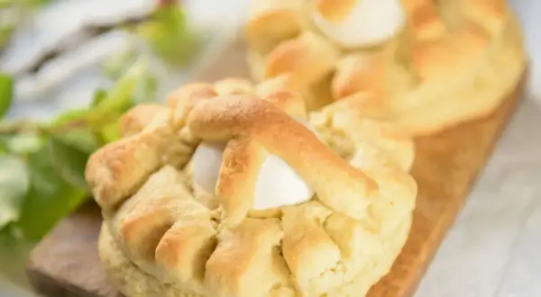 Dolci pasquali pugliesi con uova intere, decorati con impasto intrecciato, su un tagliere di legno.
