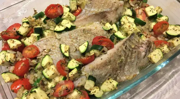 Filet de lieu noir rôti avec tomates cerises et courgettes coupées en dés, assaisonné d'herbes.