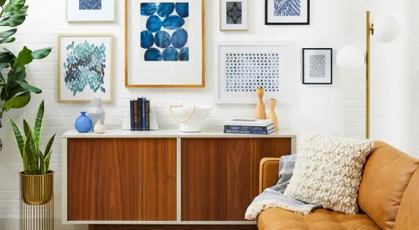 A stylish gallery wall features abstract blue art, geometric prints, and a framed textile.